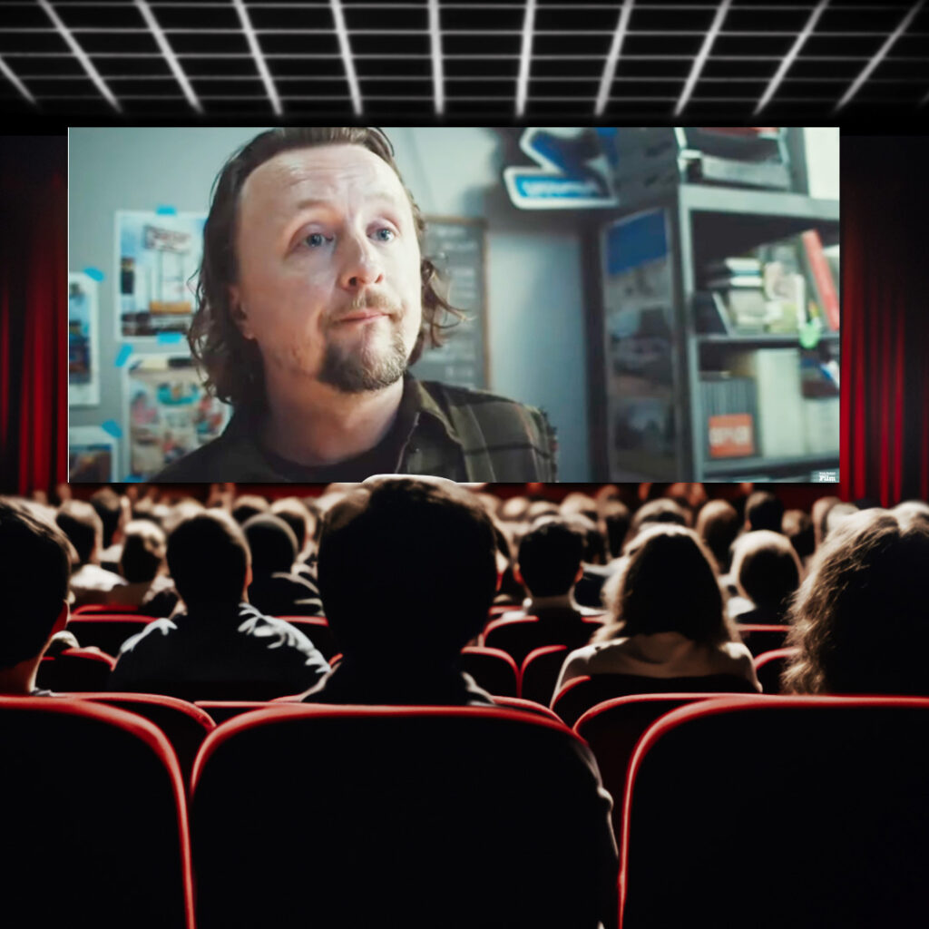 Movie theater of people looking up at the screen with actor Paul Cram's face close up from the movie "abroad"